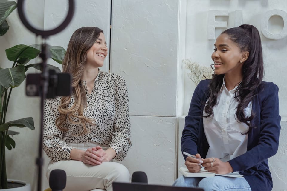 Two smiling people recording a conversation with microphones.