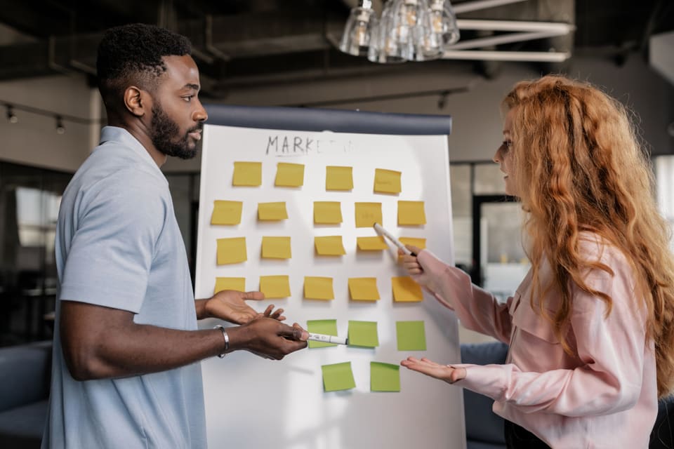 Two colleagues planning a project with notes on a whiteboard.