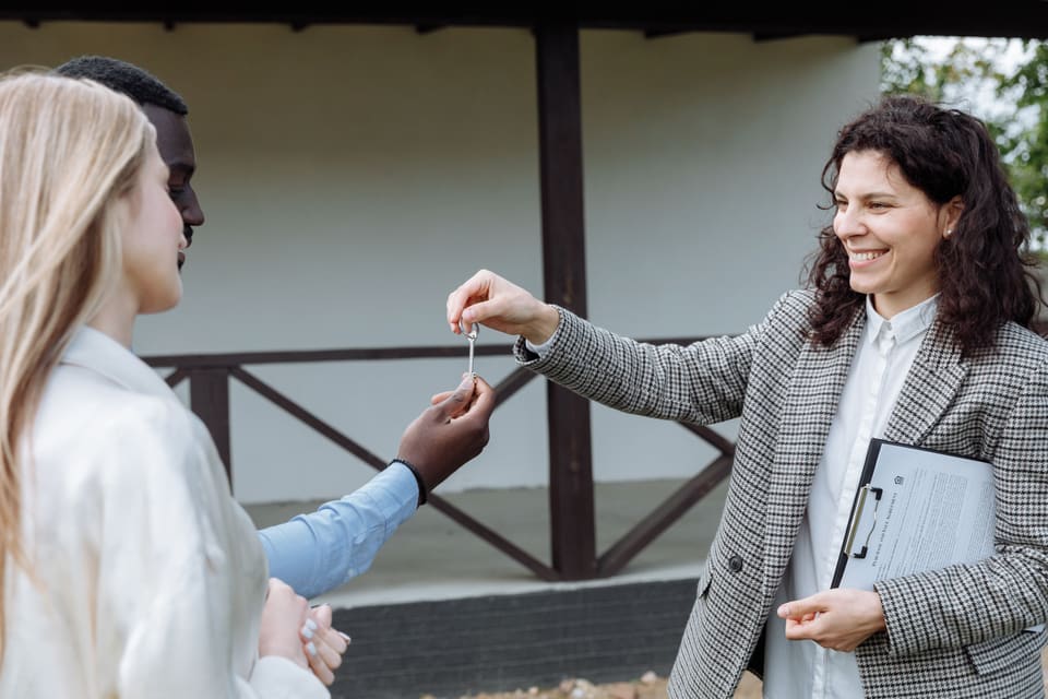 A property professional handing a key to two people outside a home.