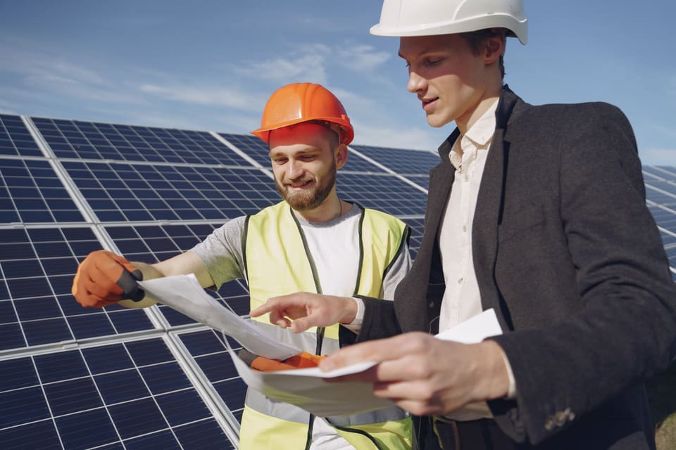 Two electrical professionals reviewing work beside solar panels.